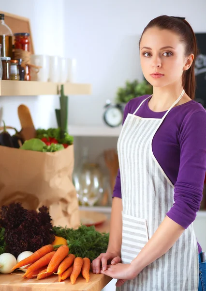 Egy fiatal nő áll a konyhájában az íróasztal mellett. — Stock Fotó