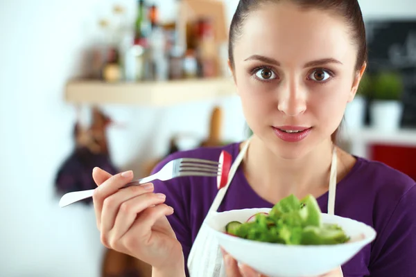 Mujer joven comiendo ensalada fresca en la cocina moderna —  Fotos de Stock