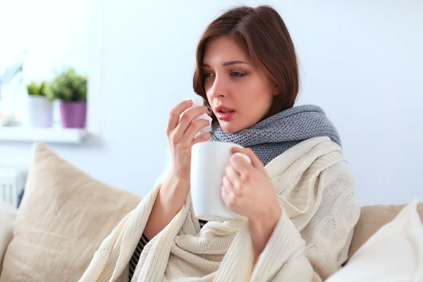 Portrait of a sick woman blowing her nose while sitting on the sofa — Stock Photo, Image