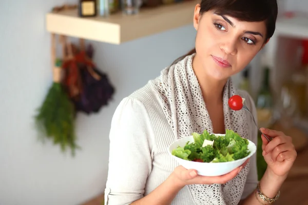 Ung kvinna äter färsk sallad i modernt kök — Stockfoto