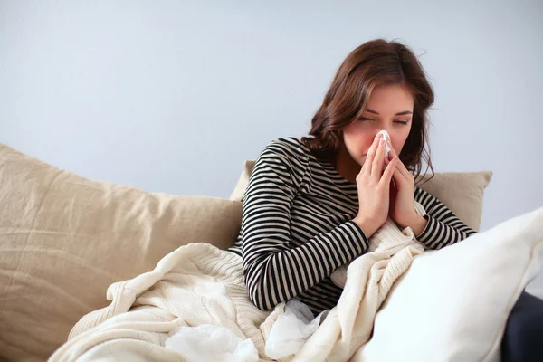 Portrait of a sick woman blowing her nose while sitting on the sofa — Stock Photo, Image