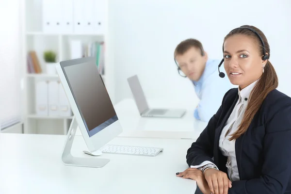 Glad kvinna bär headset och sitter på skrivbordet — Stockfoto
