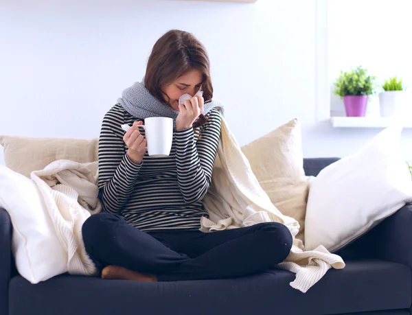Zieke vrouw bedekt met deken houden kopje thee zittend op banklaag — Stockfoto