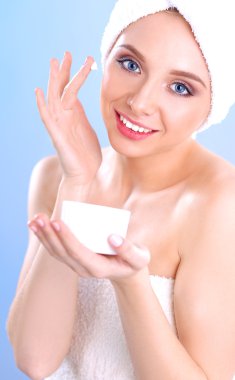 Güzel genç kadın yüzünde gri arka plan üzerinde izole bir krem uygulamak