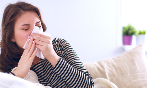 Portrait of a sick woman blowing her nose while sitting on the sofa