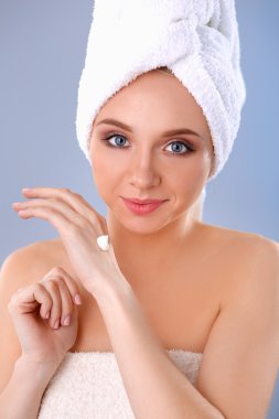 Güzel genç kadın yüzünde gri arka plan üzerinde izole bir krem uygulamak