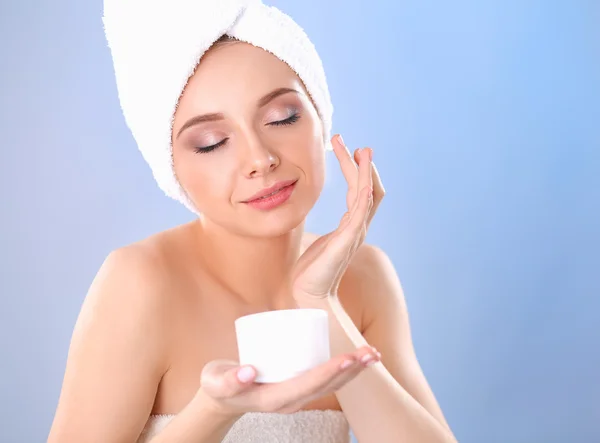 Hermosa joven aplicando una crema en su cara aislada sobre fondo gris —  Fotos de Stock