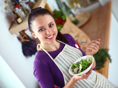 Genç kadın modern mutfakta taze salata yiyor.