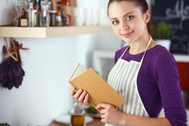 Mutfakta yemek kitabı okuyan genç bir kadın yemek tarifi arıyor.