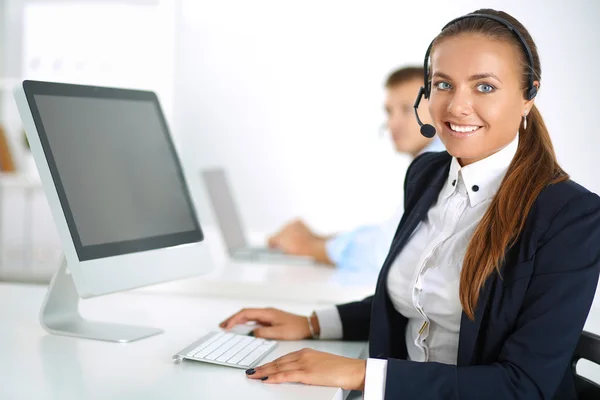 Gelukkig vrouwtje draagt een headset en zit op het bureau — Stockfoto