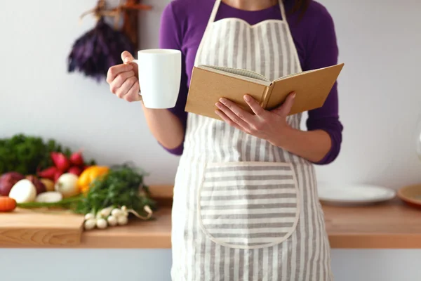 Mujer joven leyendo libro de cocina en la cocina, buscando receta —  Fotos de Stock