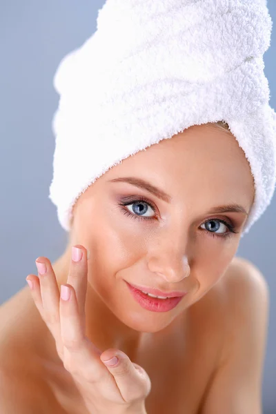 Hermosa joven aplicando una crema en su cara aislada sobre fondo gris — Foto de Stock