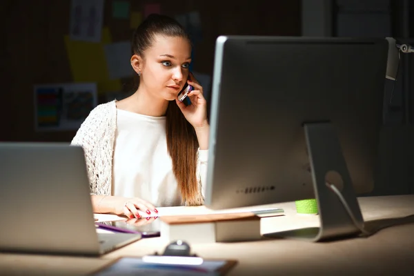 Ung kvinna som arbetar på kontor, sitter vid skrivbord och prata i telefon — Stockfoto
