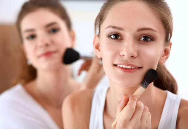 Meninas bonitas olhando no espelho e aplicando cosméticos com uma escova grande — Fotografia de Stock