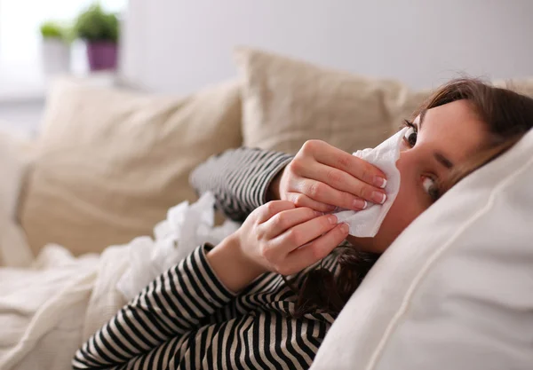 Portrait of a sick woman blowing her nose while sitting on the sofa — Stock Photo, Image