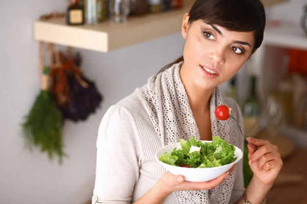 Mujer joven comiendo ensalada fresca en la cocina moderna —  Fotos de Stock