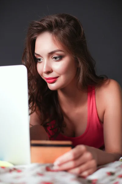 Schöne Frau mit Laptop und Kreditkarte im Bett liegend — Stockfoto