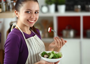 Genç kadın modern mutfakta taze salata yiyor.