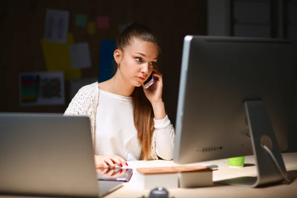 Ung kvinna som arbetar på kontor, sitter vid skrivbord och prata i telefon — Stockfoto