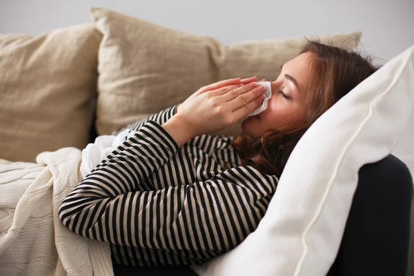 Portrait of a sick woman blowing her nose while sitting on the sofa — Stock Photo, Image