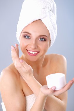 Güzel genç kadın yüzünde gri arka plan üzerinde izole bir krem uygulamak