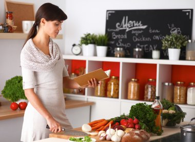 Mutfakta yemek kitabı okuyan genç bir kadın yemek tarifi arıyor.