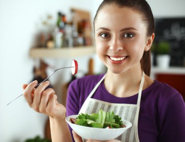 Genç kadın modern mutfakta taze salata yiyor.