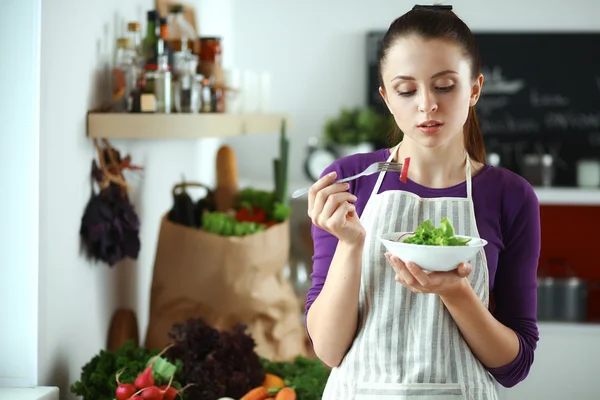 Ung kvinna äter färsk sallad i modernt kök — Stockfoto