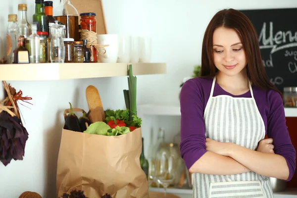 Mujer joven de pie en su cocina cerca del escritorio con bolsas de compras —  Fotos de Stock