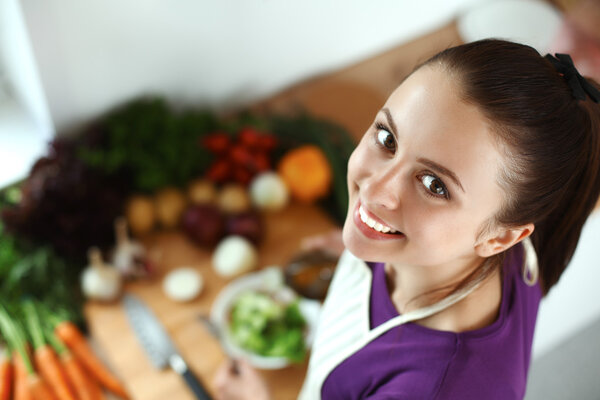 Young woman standing in her kitchen near desk with shopping bags