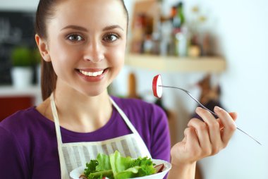 Genç kadın modern mutfakta taze salata yiyor.