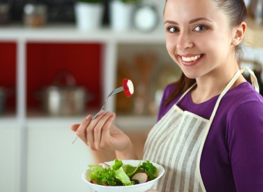 Genç kadın modern mutfakta taze salata yiyor.