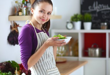 Genç kadın modern mutfakta taze salata yiyor.