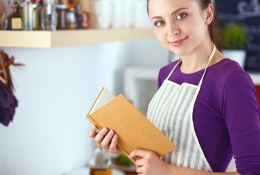Mutfakta yemek kitabı okuyan genç bir kadın yemek tarifi arıyor.