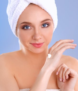 Güzel genç kadın yüzünde gri arka plan üzerinde izole bir krem uygulamak