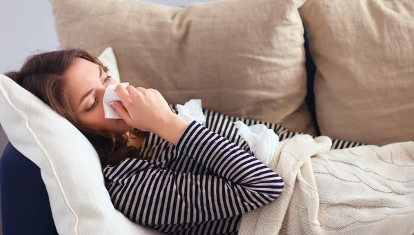 Portrait of a sick woman blowing her nose while sitting on the sofa — Stock Photo, Image