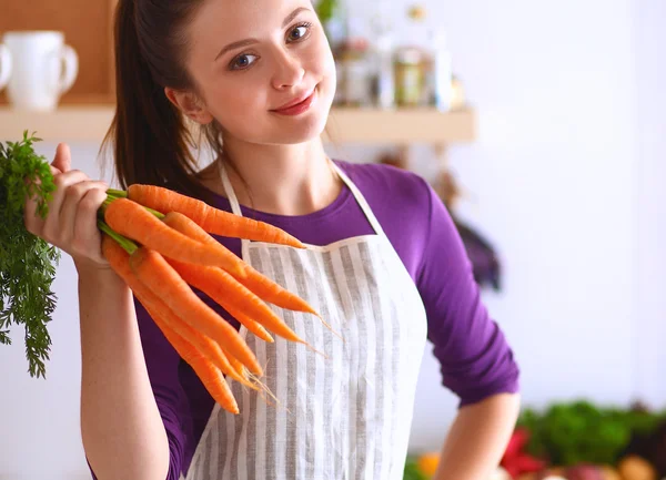 Gelukkig jong vrouw houden bos van wortelen in keuken — Stockfoto