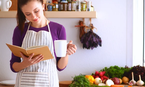 Mujer joven leyendo libro de cocina en la cocina, buscando receta —  Fotos de Stock