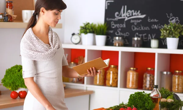 Mujer joven leyendo libro de cocina en la cocina, buscando receta —  Fotos de Stock