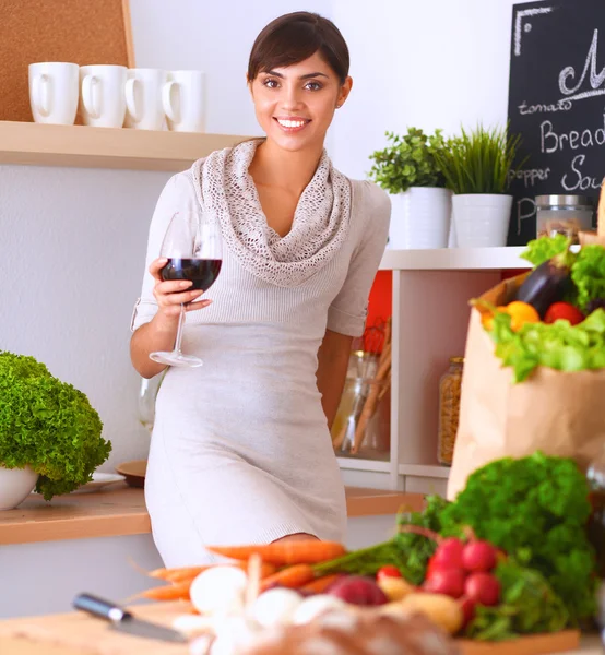 Mladá žena krájí zeleninu v kuchyni, drží sklenici vína — Stock fotografie