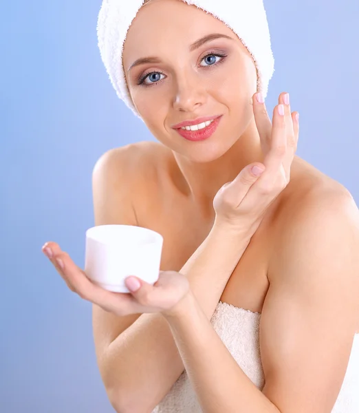 Bella giovane donna che applica una crema sul suo viso isolato su sfondo grigio — Foto Stock