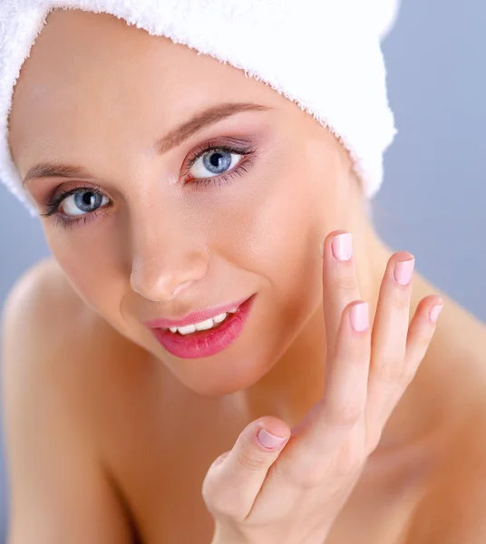 Hermosa joven aplicando una crema en su cara aislada sobre fondo gris —  Fotos de Stock