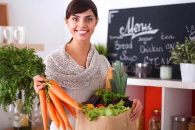 Mutfakta havuç tutan genç ve mutlu bir kadın.