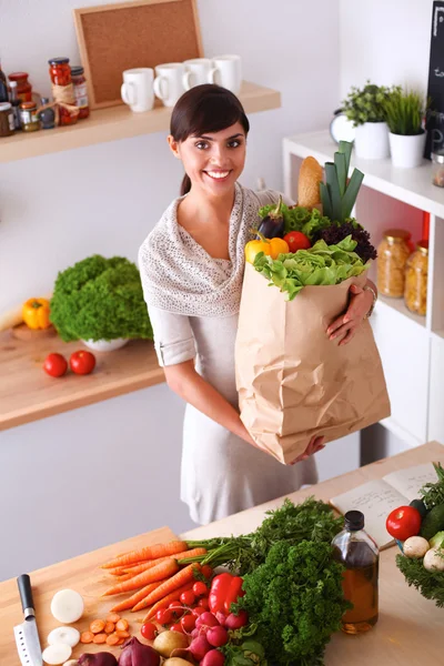 Молодая женщина держит сумку с овощами, стоящими на кухне — стоковое фото