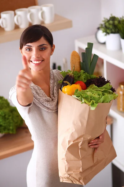 Jonge vrouw houden boodschappentas met groenten Staande in de keuken en tonen ok — Stockfoto