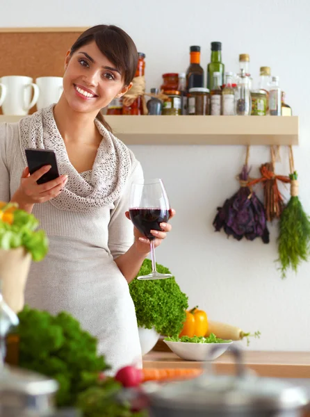 Mladá žena krájí zeleninu v kuchyni, drží sklenici vína — Stock fotografie