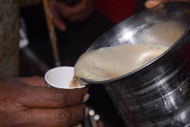 Adamın eli paslanmaz çelikten bardağa çay döküyor.