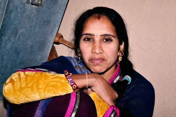 Indian rural woman is sitting in her kitchen wearing a sari.