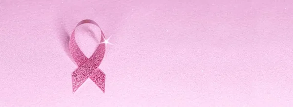 pink glittering ribbon with star shape on pink glitter banner background. breast cancer awareness symbol with copy space