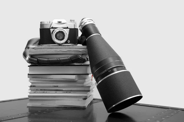 Analog camera, Photographic roll of film and a Retro Camera Lens stacked on books. Old vintage camera over stack of book. Analog film strips. Analog photography. Black and White close-up